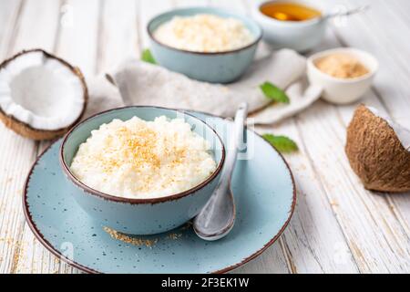 Dolce e cremoso budino di riso al cocco con miele, condito con cocco grattugiato e tostato in una ciotola in ceramica Foto Stock