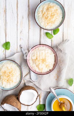 Dolce e cremoso budino di riso al cocco con miele, condito con cocco grattugiato e tostato in una ciotola in ceramica Foto Stock