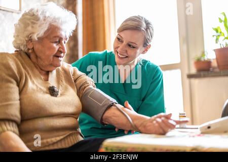 Responsabile della cura femminile che misura la pressione sanguigna della donna anziana a casa Foto Stock