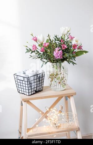 Un bouquet minimalista di tulipani bianchi, eustoma rosa, giacinto, eucalipto in vaso di vetro scanalato su una sedia. Piccoli asciugamani bianchi per le mani e il viso Foto Stock