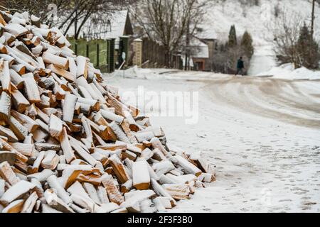 Un mucchio di legna da ardere bloccata sullo sfondo di a. strada del villaggio coperta di neve Foto Stock