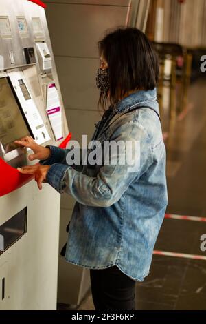 Un colpo verticale di una donna ispanica con un floreale Mascherare utilizzando un bancomat in metropolitana Foto Stock