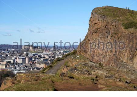 Le persone che si godono il sole e all'aperto in Holyrood Park. Da Salisbury Crags si può ammirare il Castello di Edimburgo e i tetti del centro città, Edimburgo, Scozia Foto Stock