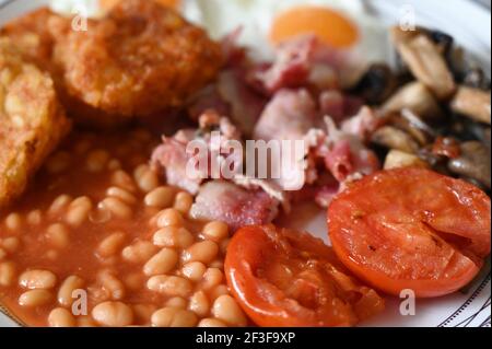 Colazione inglese tradizionale - piatto con uova fritte, fagioli, funghi, pancetta, crocchette di patate e pomodori Foto Stock