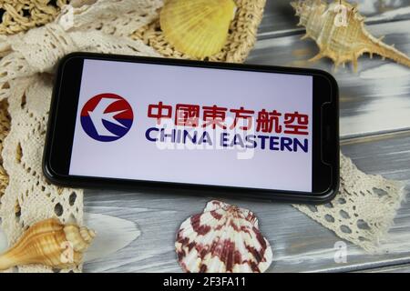 Viersen, Germania - 1 marzo. 2021: Closeup di smartphone con logo scritta delle compagnie aeree orientali della cina con cappello e conchiglie su tavolo di legno Foto Stock