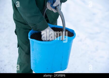 È possibile vedere da vicino come va un lavoratore manuale con un secchio blu e cospargere i marciapiedi di espanso creta così che loro non sono scivolosi nel Foto Stock