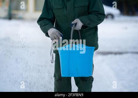 È possibile vedere da vicino come va un lavoratore manuale con un secchio blu e cospargere i marciapiedi di espanso creta così che loro non sono scivolosi nel Foto Stock