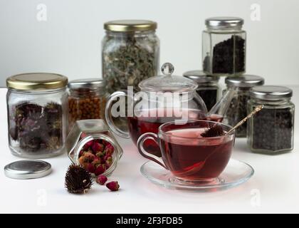 Tè alle erbe fatto in casa. Un rimedio che aumenta l'immunità e allevia lo stress. Teiera in vetro e tè con una bevanda calda e sana. Vasi trasparenti con lei asciugata Foto Stock