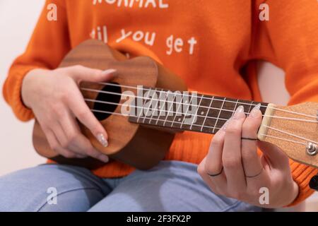 primo piano delle mani di una giovane donna irriconoscibile in sneakers che suonano l'ukulele al tramonto in città, concetto di musica amatoriale e artistica Foto Stock