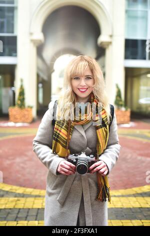 Bionda bella fotografa donna con fotocamera retrò in mano mentre scattano foto alla vecchia architettura urbana. Scopri nuovi luoghi. Foto Stock