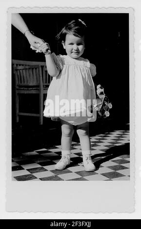 Toddler ragazza che tiene la mano della mamma nel suo vestito cute del partito. 1949, STATI UNITI Foto Stock