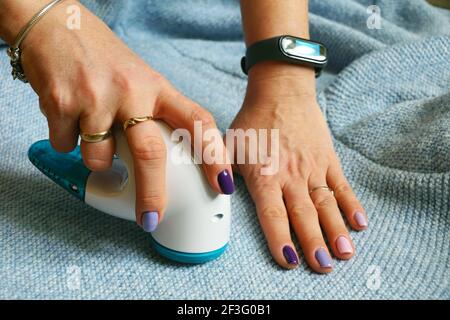Dispositivo wireless per la pulizia di tessuti a maglia da lanugine. La donna sta rimuovendo il lanugine dal maglione. Foto Stock