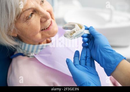 Dentista che confronta l'impronta dentale con la mascella della donna anziana Foto Stock