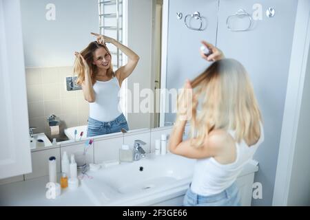 Giovane donna allegra con spray per capelli in bagno Foto Stock