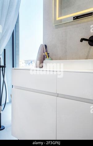 Interni moderni del bagno con un lavandino bianco sulla parte superiore di un ripiano bianco e uno specchio appeso sopra di esso. Foto Stock