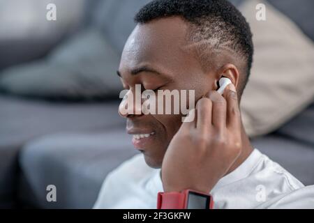 Ragazzo afroamericano in abiti bianchi che indossa auricolari wireless Foto Stock
