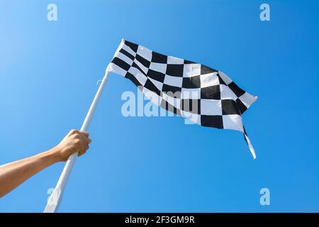 Mano che tiene bandiera a scacchi su sfondo blu cielo Foto Stock