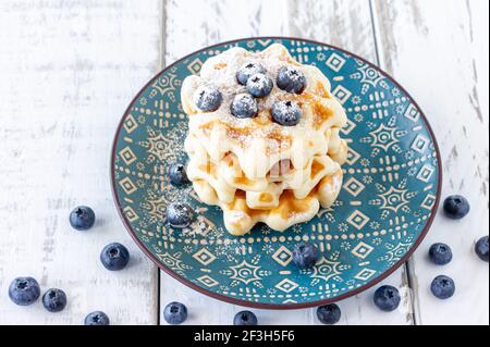 I classici waffle belgi fatti in casa sono ricoperti di mirtilli freschi e polvere di zucchero su un piatto. Foto Stock