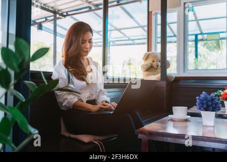 Giovane ragazza d'affari asiatica che lavora con il computer portatile nel caffè, donna freelance che si collega a internet via computer. Foto Stock