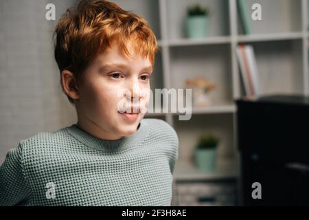 Primo piano ritratto di allegro ragazzo rosso reckled seduto tavolo e guardando via Foto Stock