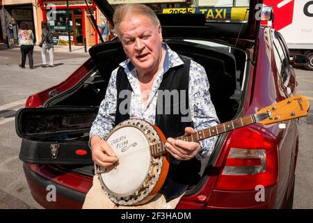 Il tassista irlandese è seduto nel bagagliaio della sua auto a giocare un banjo in attesa di tariffe al posteggio dei taxi College Street a Killarney, County Kerry, Irlanda Foto Stock