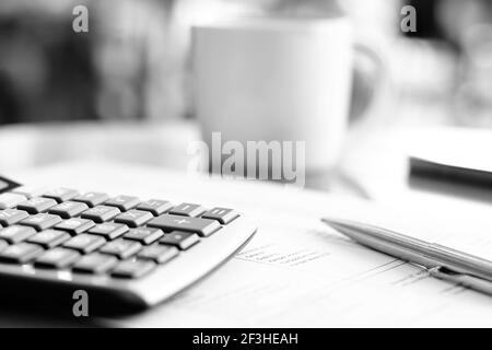 calcolatrice e penna sulla carta sul tavolo con sfocatura sfondo della tazza di caffè - effetto monocromatico Foto Stock