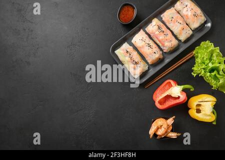 Involtini primaverili asiatici con verdure colorate, gamberi avvolti in carta di riso su sfondo nero con spazio per la copia. Vista dall'alto. Foto Stock