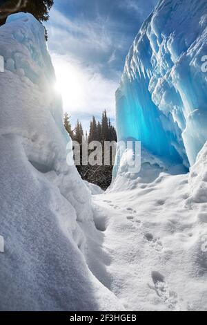 Cascata di montagna ghiacciata con ghiaccio contro il cielo blu e la foresta sullo sfondo Foto Stock