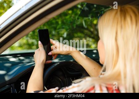 Femmina giovane conducente utilizzando il touch screen smartphone e la navigazione gps in un'auto. Foto Stock