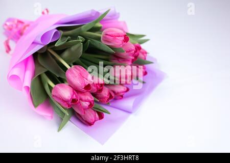 un bouquet di tulipani natalizi confezionati in rosa il legatore giace su un tavolo bianco Foto Stock