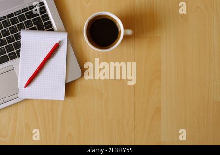 Lavoro da casa. Set da ufficio con computer portatile, notebook, caffettiera, penna su tavolo di legno. Concetto aziendale. Spazio per la copia della vista dall'alto piatto. Foto Stock