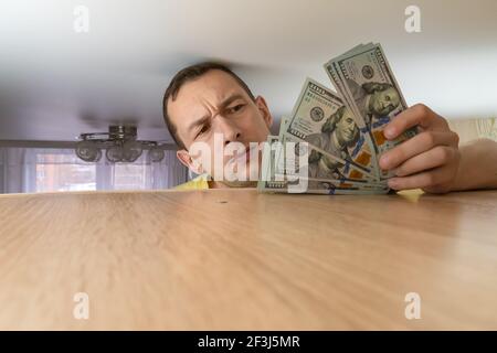 L'uomo tiene il risparmio del dollaro nascosto su un armadietto nelle sue mani. Risparmio di denaro in tempi difficili Foto Stock