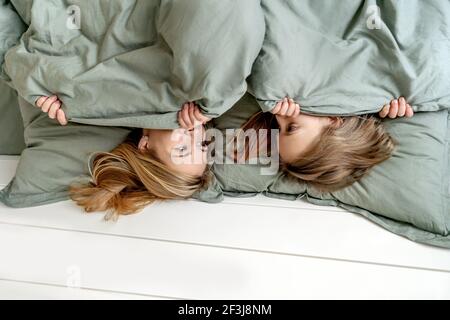 Donna con bambina si nasconde sotto coperta. Mattina, madre e figlia si divertono. Concentrarsi sugli occhi del donna. Foto Stock