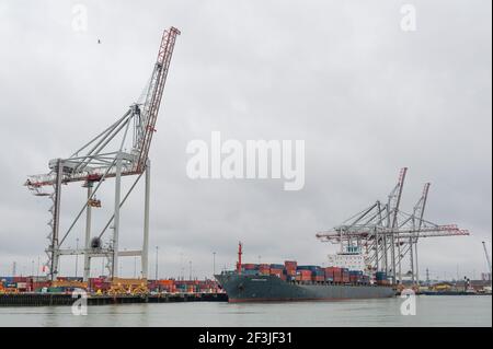 Southampton, Regno Unito, 04 Mar 2021. I cieli sovrastanti offrono uno sfondo cupo a parte del cantiere navale di Southampton, dove una nave da carico caricata con contenitori di trasporto in metallo è ormeggiata accanto a gru da cantiere gigantesche. Le banchine di Southampton hanno recentemente ottenuto lo status di porto libero. Foto Stock