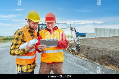 Due operai edili che utilizzano un computer tablet durante lo sviluppo di strade cantiere Foto Stock