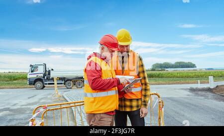 Due operai edili impegnati nella pianificazione dei cantieri con computer tablet online in internet Foto Stock