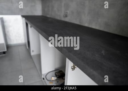 Piano di appoggio grigio scuro installato su una cucina personalizzata. Cucina modulare grigia in materiale truciolare in varie fasi di installazione. Tavolo da cucina Foto Stock