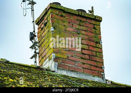 Vecchio camino stack su un tetto di casa coperto di muschio e licheni che hanno bisogno di riparazione e di rimetterne immagine foto stock cemento mortaio Foto Stock