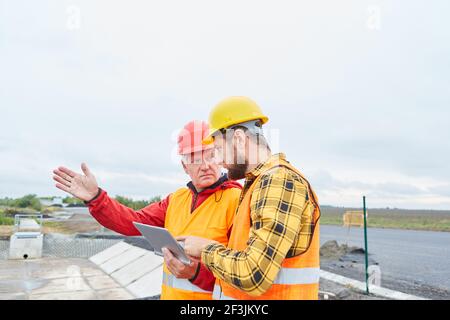 Architect discute la pianificazione della costruzione di strade con il caposquadra che utilizza un computer tablet Foto Stock