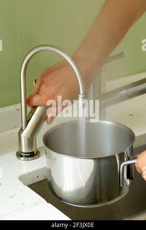 Donna che riempie la pentola con acqua Foto Stock