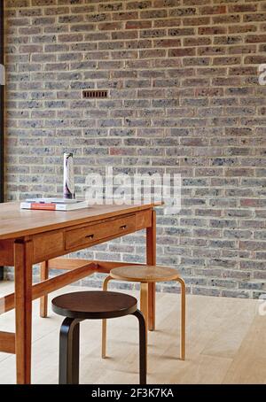 Duggan Morris House: Kings Grove, Peckham, Londra. La fotografia mostra l'area salotto al primo piano che mostra sgabelli non abbinati e una scrivania/tavolo in legno Foto Stock