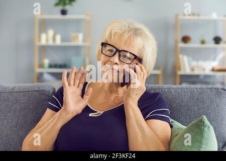 Sorridente anziana nonna bionda che parla con i bambini su smartphone o un amico a casa Foto Stock