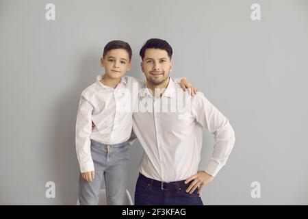 Positivo padre e figlio in eleganti camicie bianche e jeans stare in piedi e guardare la fotocamera Foto Stock