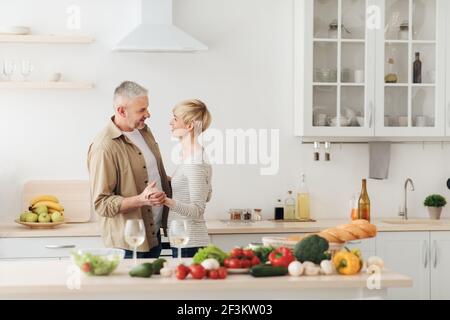 Felice coppia senior innamorata che celebra la giornata di San Valentino a casa insieme, gustando una cena romantica Foto Stock