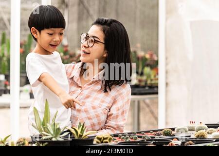 Una madre e un figlio asiatici hanno scelto e comprato felicemente il cactus sulla fattoria di Cactus. Stagione di piantare alberi. Autentica famiglia asiatica. Foto Stock