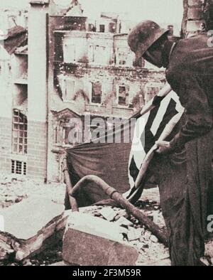 Foto d'archivio del soldato tedesco catturato solleva una bandiera nazista dai detriti di Berlino. 1945 Foto Stock