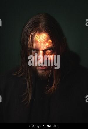 Un uomo demone con una faccia ardente in un fuoco Scintille e fumo su sfondo verde scuro horror diavolo di Halloween Foto Stock