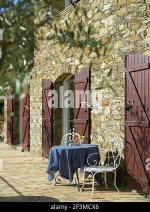 Tradizionale esterno in pietra con persiane doppie aperte e tavolo per due con tovaglia e sedie in metallo ornato, Francia. Foto Stock