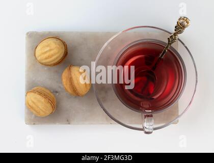 Biscotti fatti in casa a forma di noce ripieni di latte condensato in un vaso di vetro su un tagliere di marmo. Tè rosso sudanese alle rose in una tazza e teiera. Foto Stock