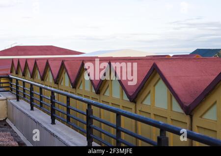 Una serie di cabine da spiaggia rosse e gialle dietro un recinto in acciaio sulla costa mediterranea (Pesaro, Italia, Europa) Foto Stock
